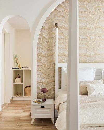 Arched doorway leads to a bedroom with wave-patterned wallpaper, a white four-poster bed, and a small nightstand.
