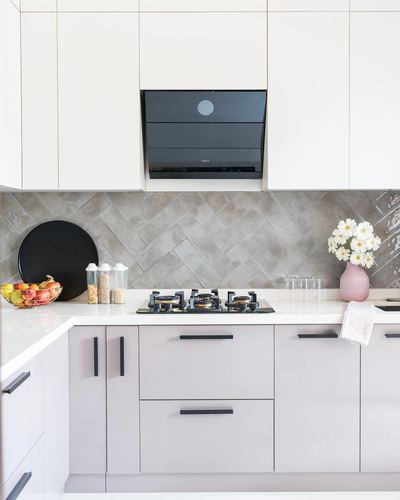 Corner kitchen with white cabinetry, herringbone backsplash tile, and black chimney hood over hob