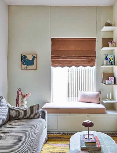 Sage-green living room with terracotta roman blind, built-in window seat, striped sofa, and shelving with decor.