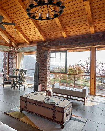 Rustic farmhouse living room with exposed brick pillars, wood beam ceiling, trunk coffee table and valley view