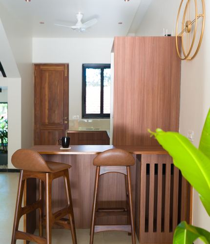 Wooden breakfast counter with two leather-seated stools beside a fluted cabinet and window view.