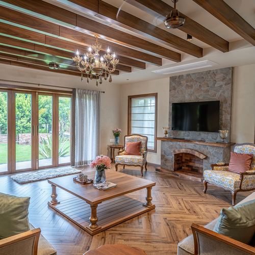 Living room with wood beam ceiling, stone fireplace, chandelier, and herringbone wood floor opening to garden