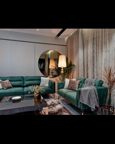 Living room with two emerald velvet sofas, round mirror, and sheer curtained window at dusk