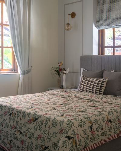 Bedroom with fluted grey headboard, floral bedspread, brass sconce and wooden windows in Goan villa
