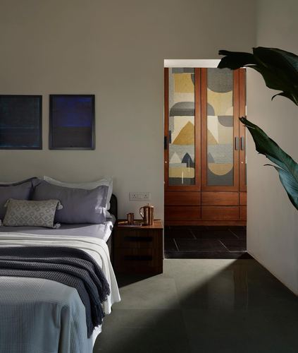 Bedroom with grey linens, wooden nightstand, and view through doorway to a patterned wardrobe.