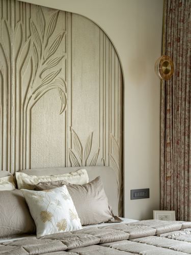 Arched carved headboard with leaf motif behind layered beige and pink bedding