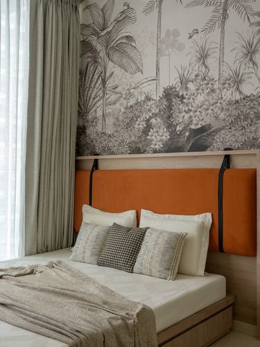 Bed with orange velvet headboard suspended by leather straps below a black-and-white botanical mural