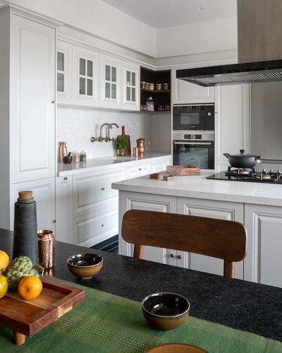 White kitchen with island, black stone countertop, copper vessels and wooden chair in foreground