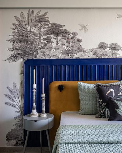 Bedroom with fluted navy headboard, mustard velvet cushion, and forest mural wallpaper