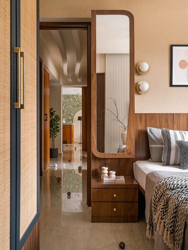 Bedroom with curved wood-framed mirror, cane door, and view through doorway into a mural-papered hallway