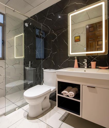 Bathroom with black veined stone wall, backlit square mirror, floating vanity, and glass shower.