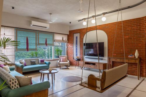Living room with teal sofas, hanging wooden swing, and curved exposed brick wall with tv niche