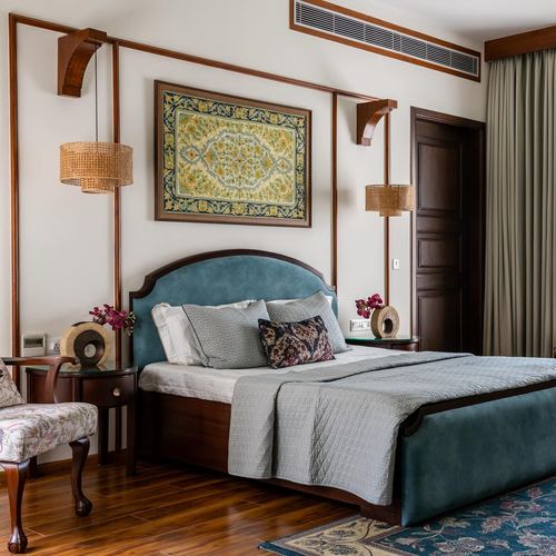 Bedroom with teal velvet headboard, wood paneling, cane pendant lights, and framed textile art