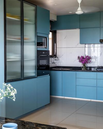 Teal blue modular kitchen with reeded glass cabinet, marble-look backsplash, and black countertop