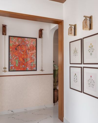 Foyer with Kerala mural painting, brass hanging lamps, and gallery wall of botanical prints beside an archway.