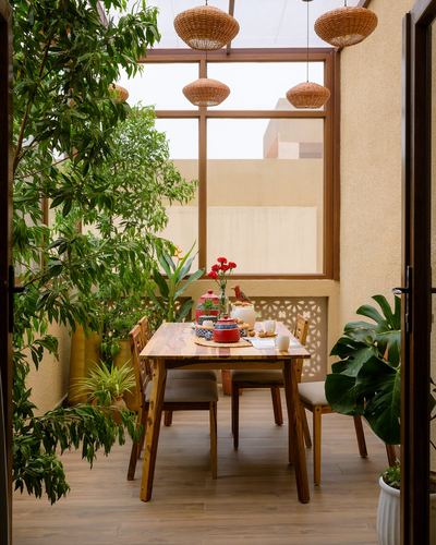 Sunlit dining nook with wooden table, cane chairs, woven pendants, and lush potted plants