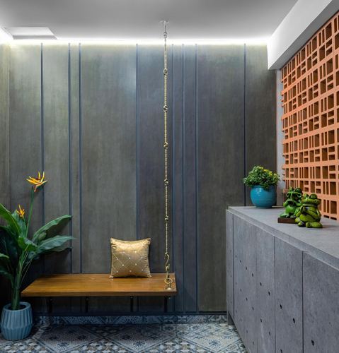 Entryway with hanging wooden swing, fluted grey wall, terracotta jaali screen and patterned floor tiles
