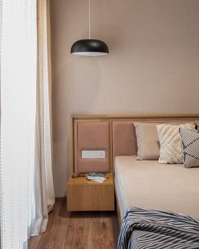 Bedroom corner with dome pendant light, floating wood nightstand, and upholstered headboard against earthy plaster wall.