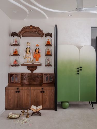 Carved wooden pooja unit with deity idols beside a tall arched green cabinet
