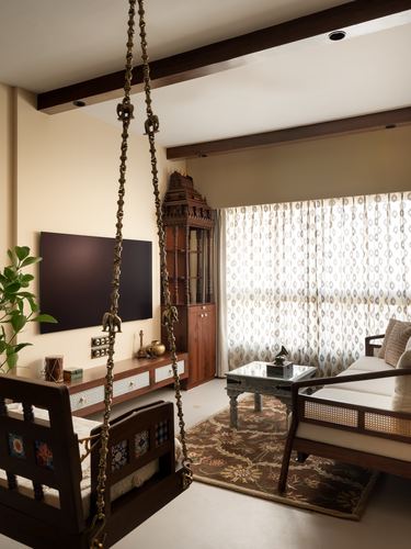 Living room with carved wooden swing, tv console, brass details, and patterned curtains lit by daylight