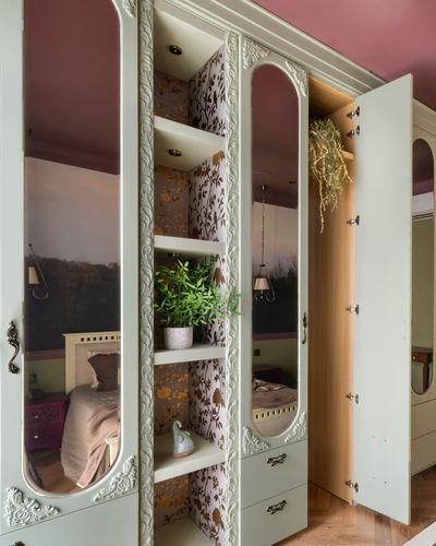 Open sage-green French-style wardrobe with mirrored doors and floral wallpapered shelving