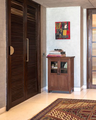 Foyer corner with louvered wooden doors, glass cabinet, framed artwork, and patterned runner rug