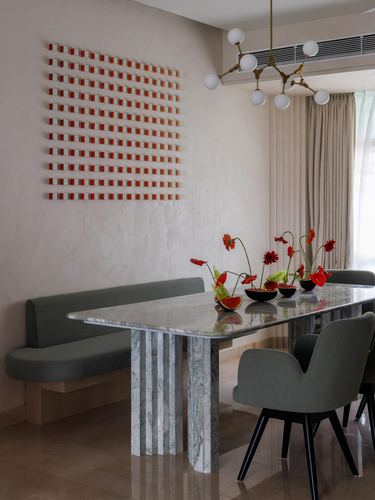 Dining area with marble table, sage banquette, brass pendant light and red floral art on textured wall