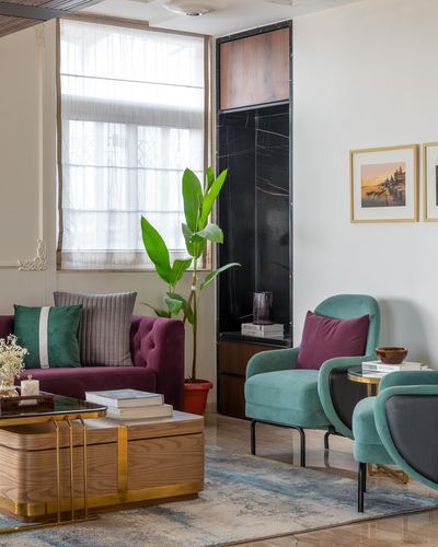Living room corner with maroon tufted sofa, teal armchairs, and a black marble niche wall