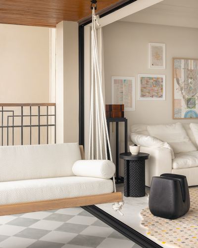 White cushioned hanging daybed on balcony opening into living room with gallery wall and white sofa