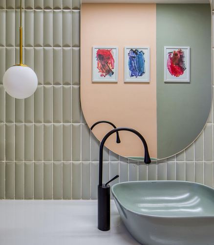 Green-tiled bathroom with peach-green pill mirror, framed art, globe pendant, and sculptural sink