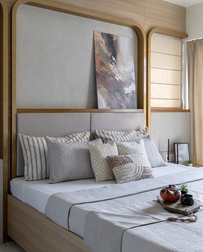 Bedroom with beige upholstered headboard, arched brass frame, abstract painting, and layered cushions