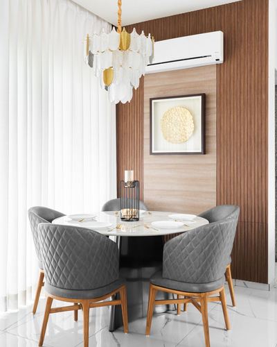 Round marble dining table with grey velvet chairs beneath a layered glass chandelier