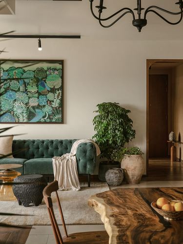 Living room with green tufted sofa, live-edge wood table, plants and botanical art under a black chandelier