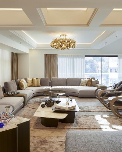 Living room with curved beige sofa, layered coffee tables, and gold leaf chandelier under coffered ceiling
