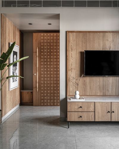 Foyer with carved wooden door beside living room wall-panelled tv unit and console