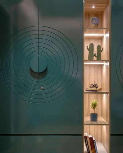 Teal cabinet door with concentric circle pattern beside lit wooden shelves with decor objects