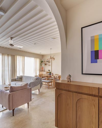 Living room seen through ribbed archway with wood sideboard, art print, and sunlit sofas beyond