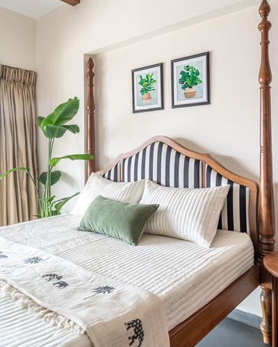 Colonial-style bedroom with carved wooden four-poster bed, striped headboard, and botanical wall art