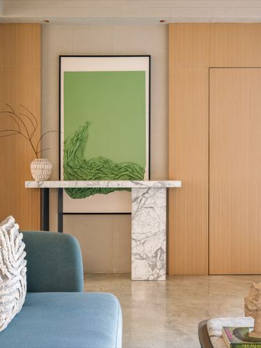 Marble console table beneath green textile artwork against fluted wood wall, teal armchair in foreground