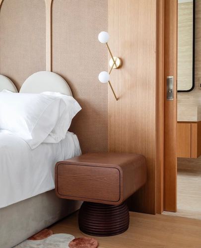Bedroom corner with cane headboard, brass double-globe sconce, and rounded wooden nightstand beside a sliding door