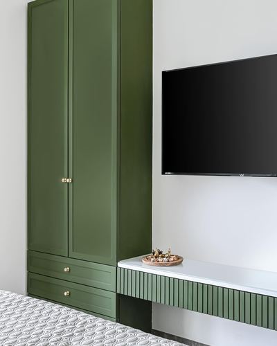 Green paneled wardrobe beside wall-mounted TV over a fluted green floating console in a bedroom