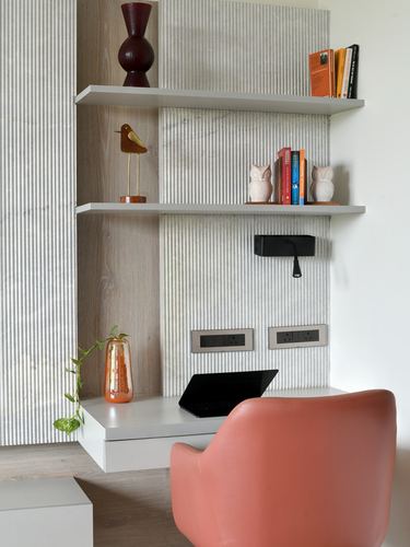 Study nook with floating shelves, ceramic decor, and a coral leather chair against a ribbed textured wall