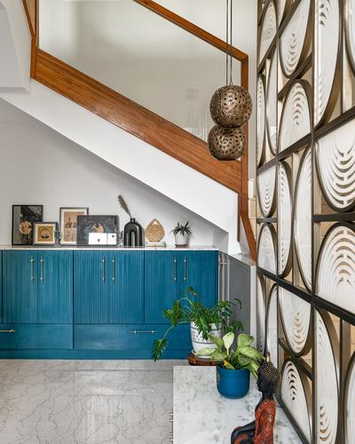 Teal cabinetry under a wooden staircase beside a carved perforated screen divider