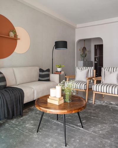 Neutral living room with striped armchairs, beige sofa, and round wood coffee table beneath circular wall art