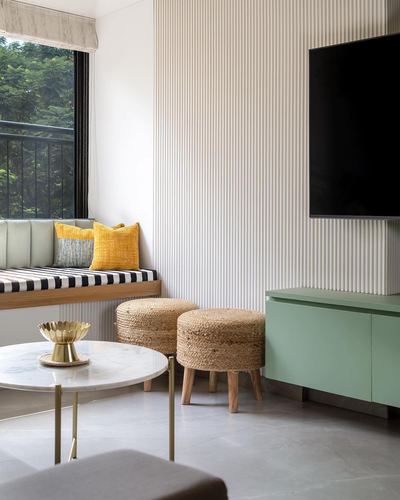 Living room corner with fluted wall panel, mint tv unit, jute pouffes and window seat with mustard cushions