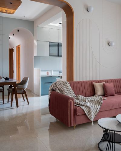 Living room with pink channel-tufted sofa framed by a wooden arch opening to kitchen and dining