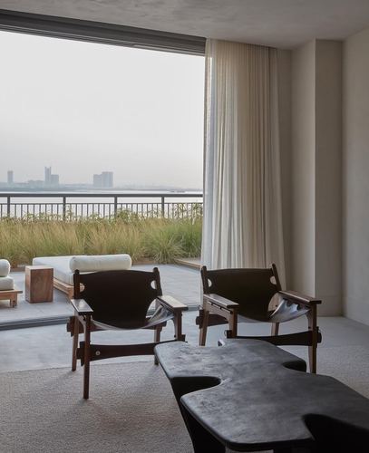 Two dark leather sling chairs face a sculptural black bench, sheer curtain beside a terrace overlooking the Dubai skyline