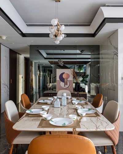 Marble dining table with tan leather chairs beneath a brass globe chandelier in a mirrored dining room