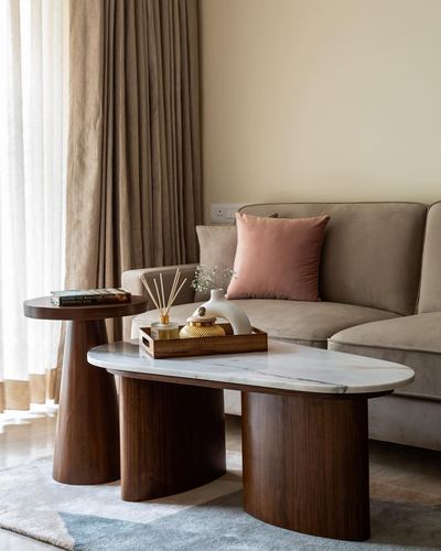 Living room corner with marble-top coffee table on cone legs, side table, and beige sofa with pink cushion