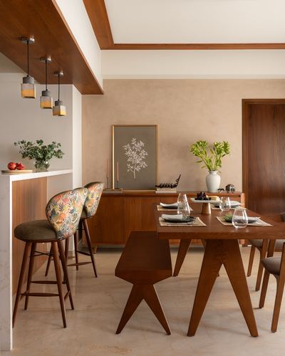 Warm-toned dining and breakfast counter with wood table, patterned stools, and pendant lights